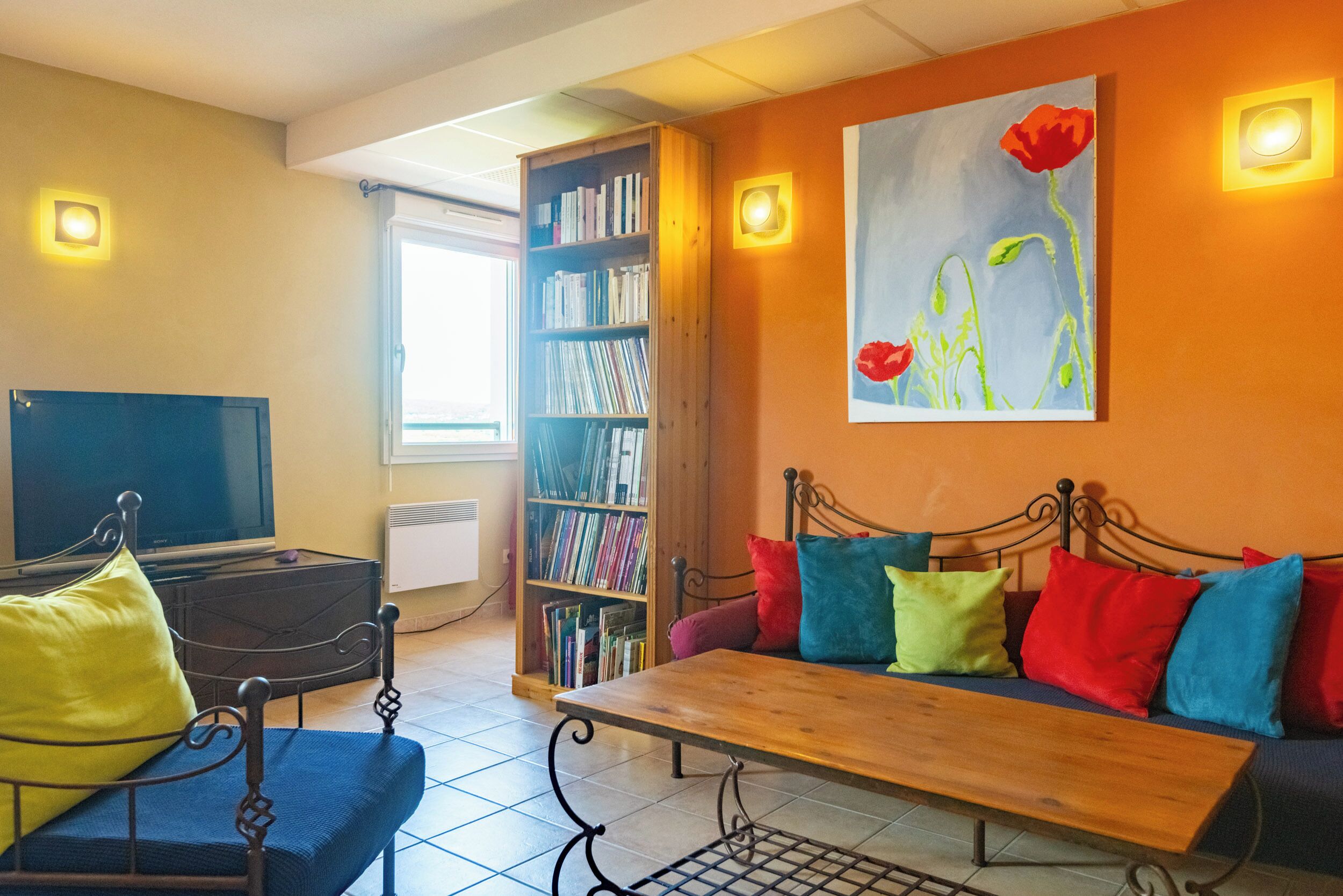 Un salon avec un canapé, une table basse, un téléviseur, une bibliothèque et un tableau accroché au mur.