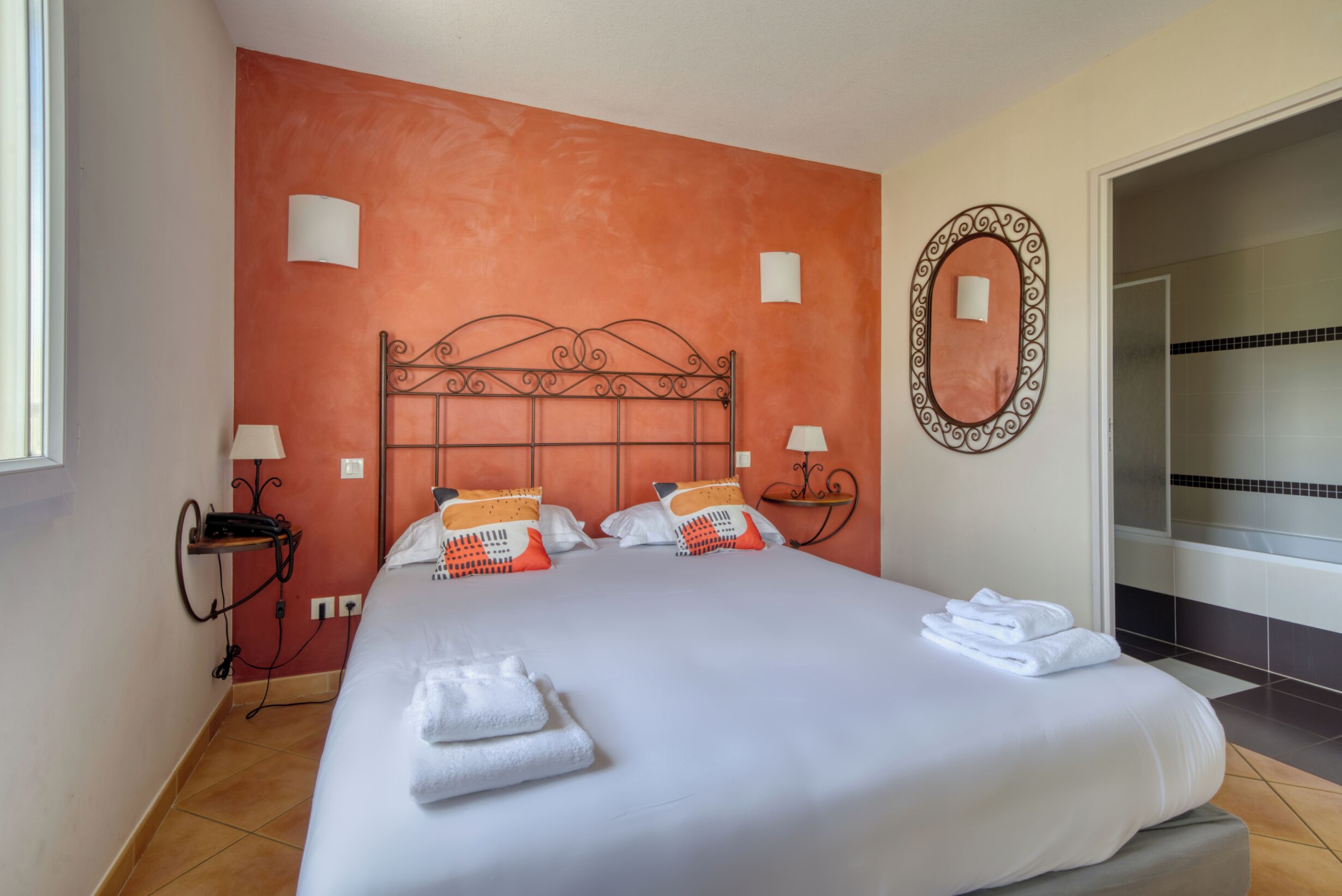 A hotel room with a large bed, two bedside tables, a mirror, and a view of a bathroom.