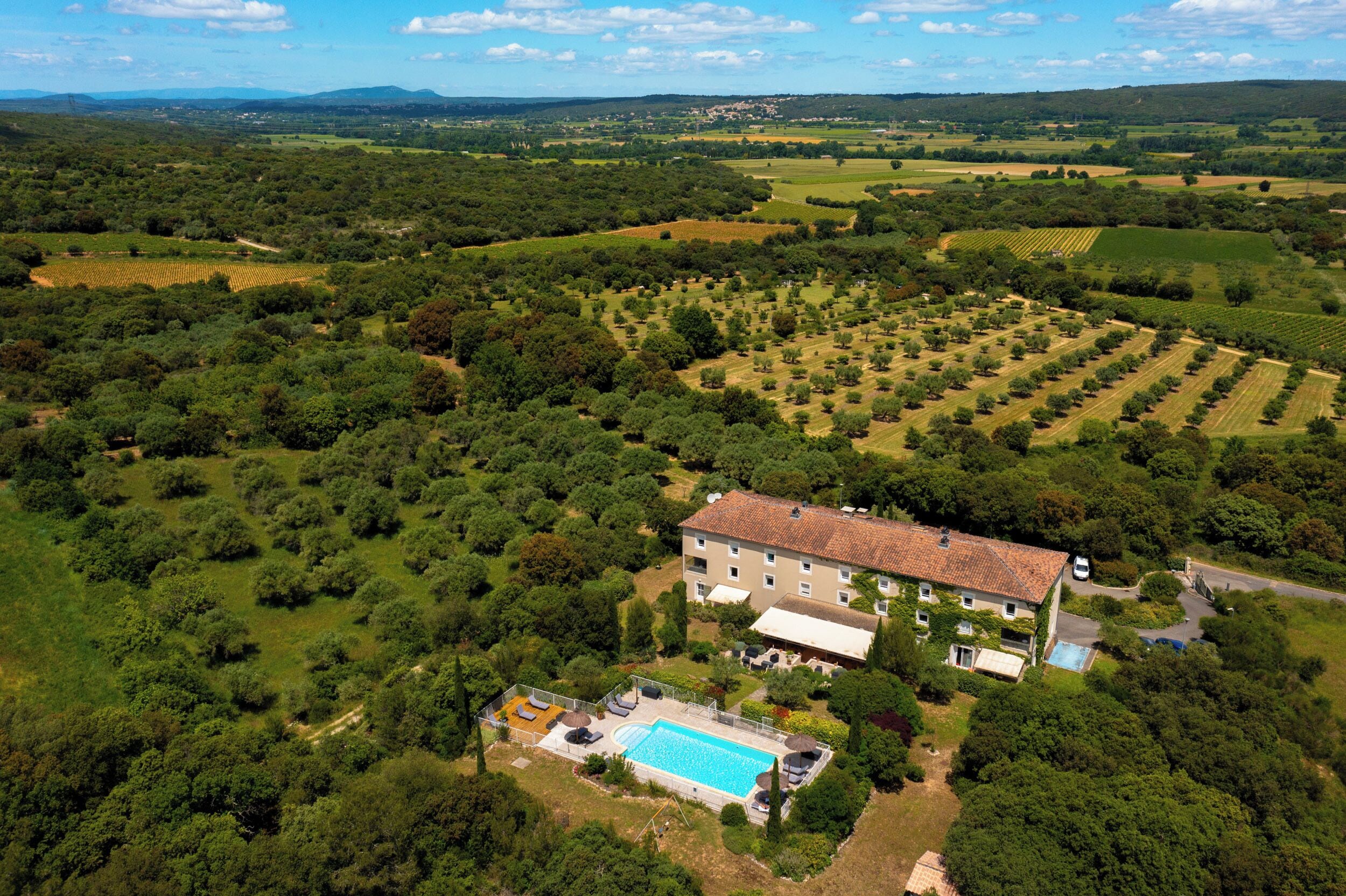 A large villa with a swimming pool, surrounded by lush greenery and agricultural fields.