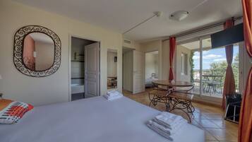A hotel room with a bed, a round mirror, a balcony with a table and chairs, and a view of the outdoors.