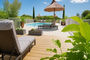 Un espace aménagé au bord de la piscine, avec des chaises longues, des jardinières et un parasol en chaume.
