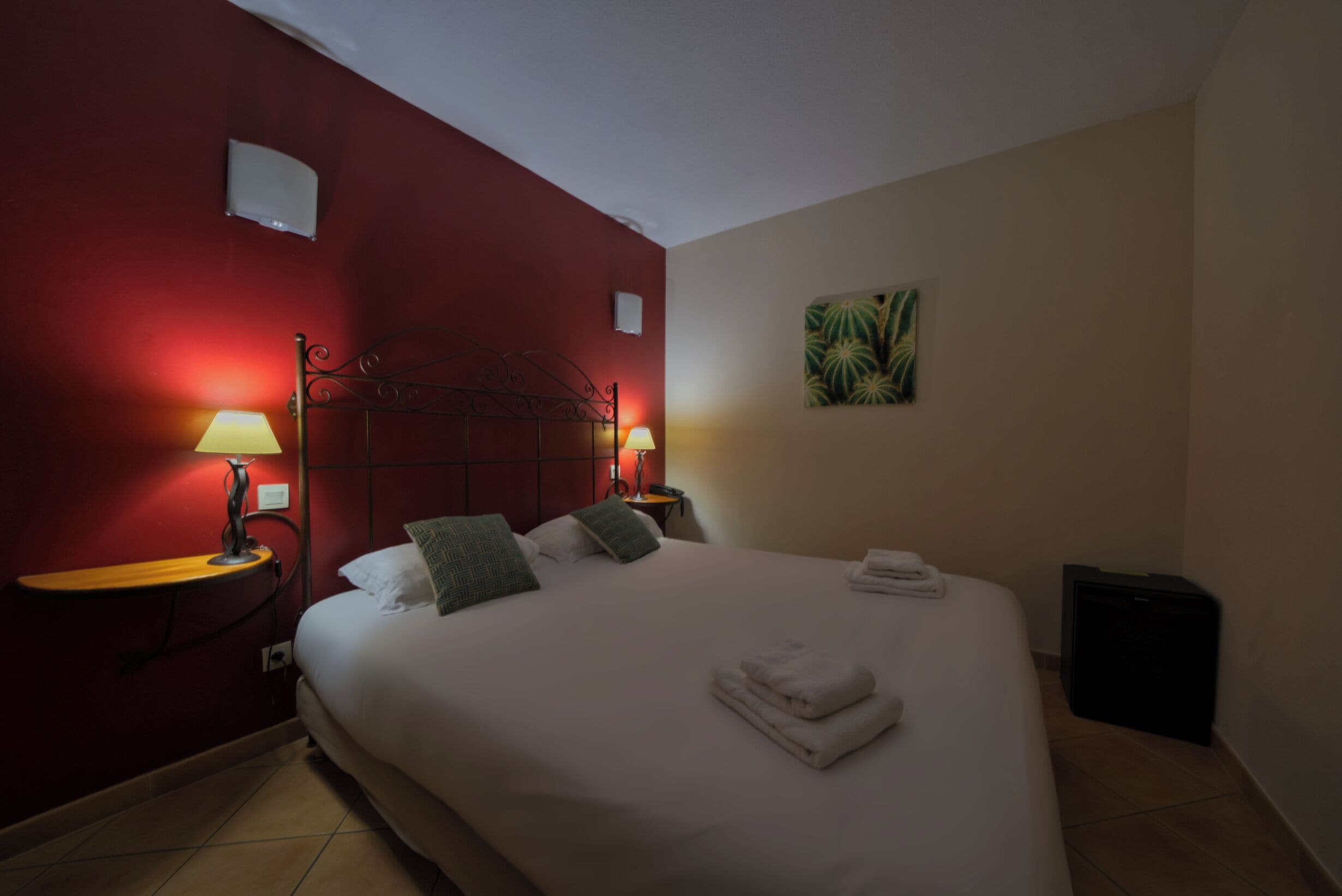 A hotel room with a large bed, two bedside lamps, a small table, and a wall-mounted picture.