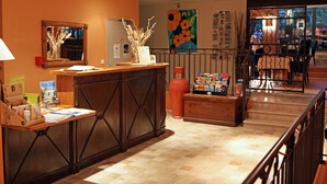 Zona de recepción con un mostrador de madera, un tablón de anuncios y una escalera que sube a otro piso.