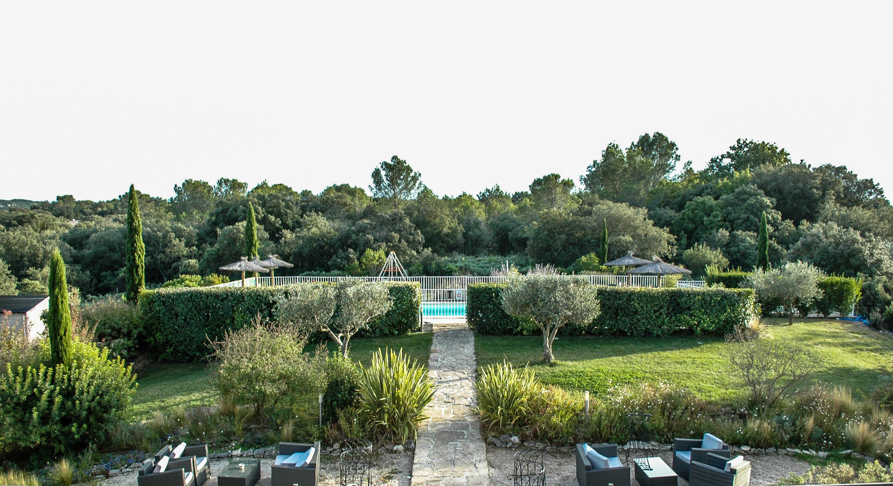 Un jardin aménagé avec un sentier en pierre menant à une piscine, le tout entouré de haies soigneusement taillées et de diverses plantes.