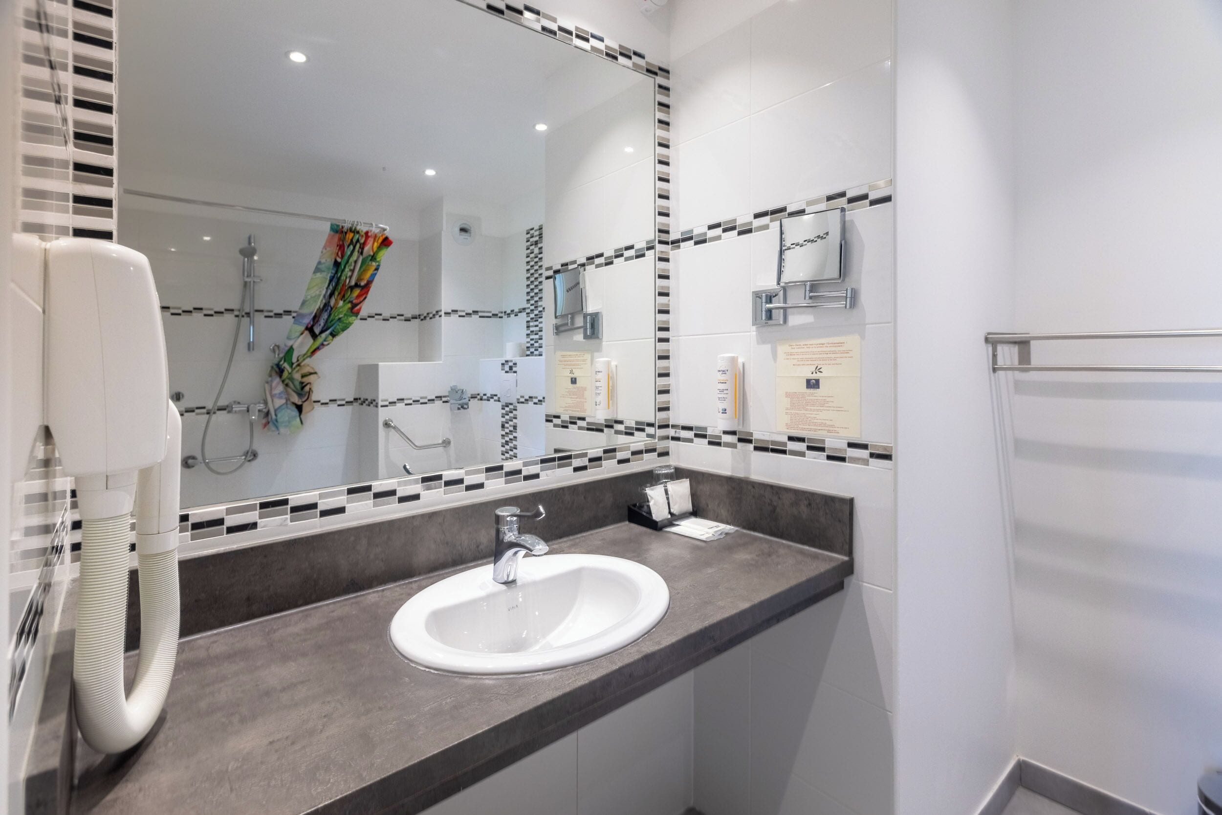 A modern bathroom with a white sink, a large mirror, and a shower area.