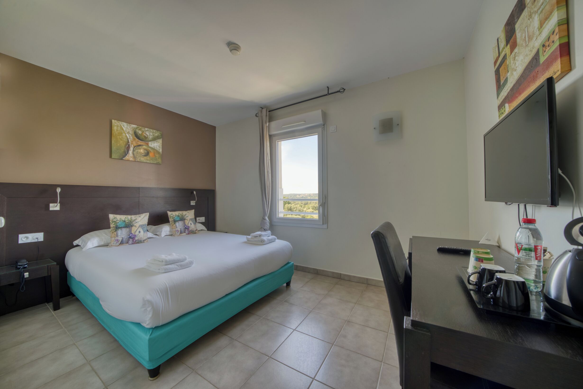 A hotel room with a bed, a desk, a television, and a window with a view.