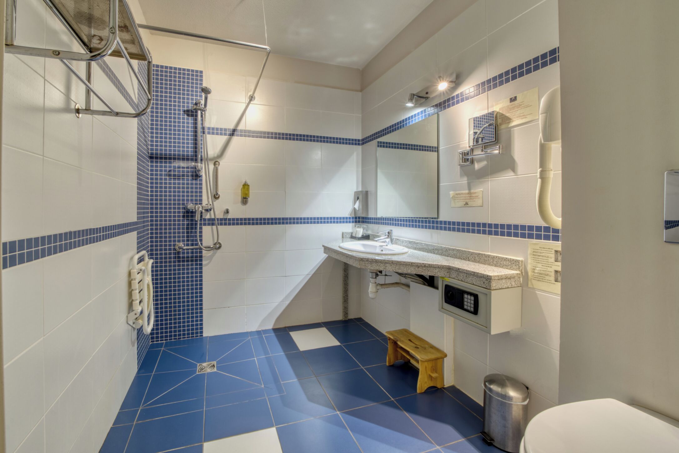 A bathroom with a shower, sink, mirror, and a small wooden stool.