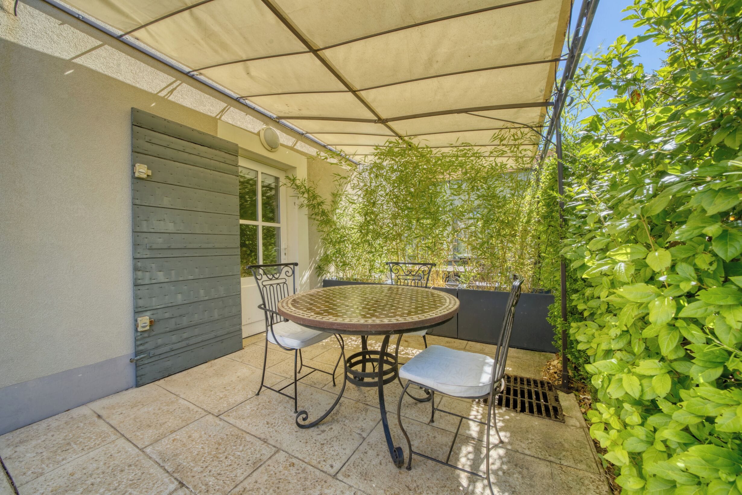 An outdoor patio with a round table and chairs, a covered area, and a wall with a door.