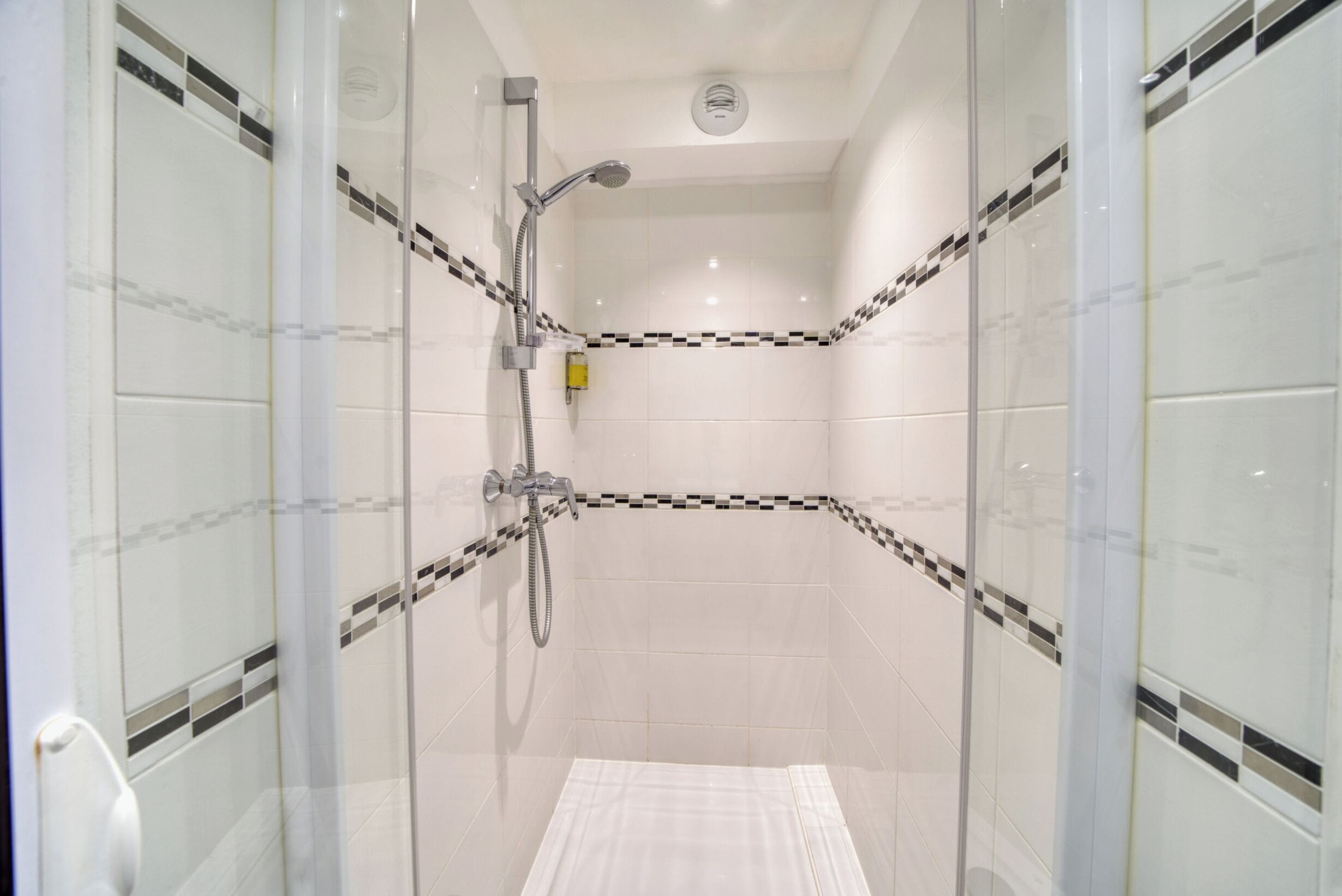 A glass-enclosed shower room with a handheld showerhead and a wall-mounted faucet.