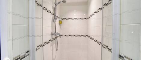 A glass-enclosed shower room with a handheld showerhead and a wall-mounted faucet.