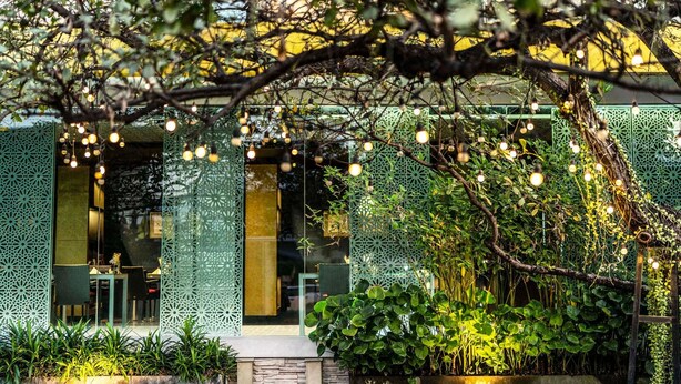 Un área de estar al aire libre con una mesa y sillas, rodeada de exuberante vegetación e iluminación decorativa.