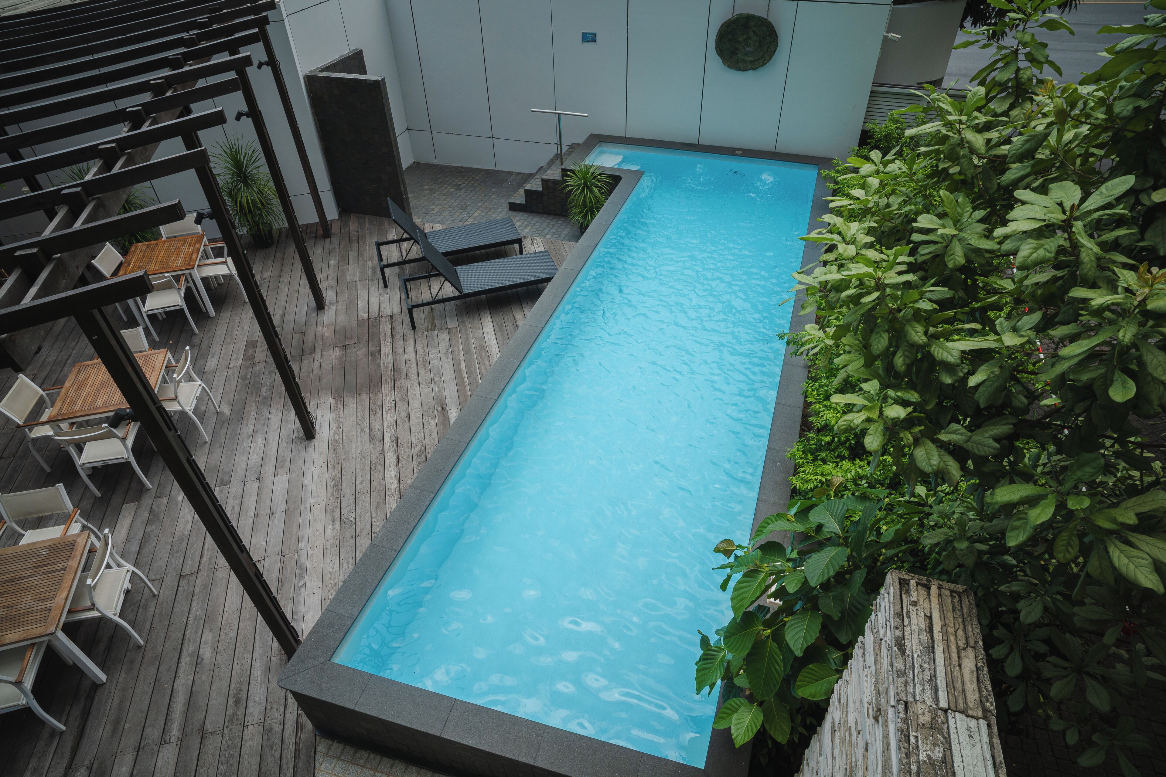 A rectangular pool with a wooden deck and lounge chairs.