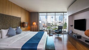 Una habitación de hotel moderna con una cama grande, vistas a la ciudad, un televisor de pantalla plana y un área de descanso.
