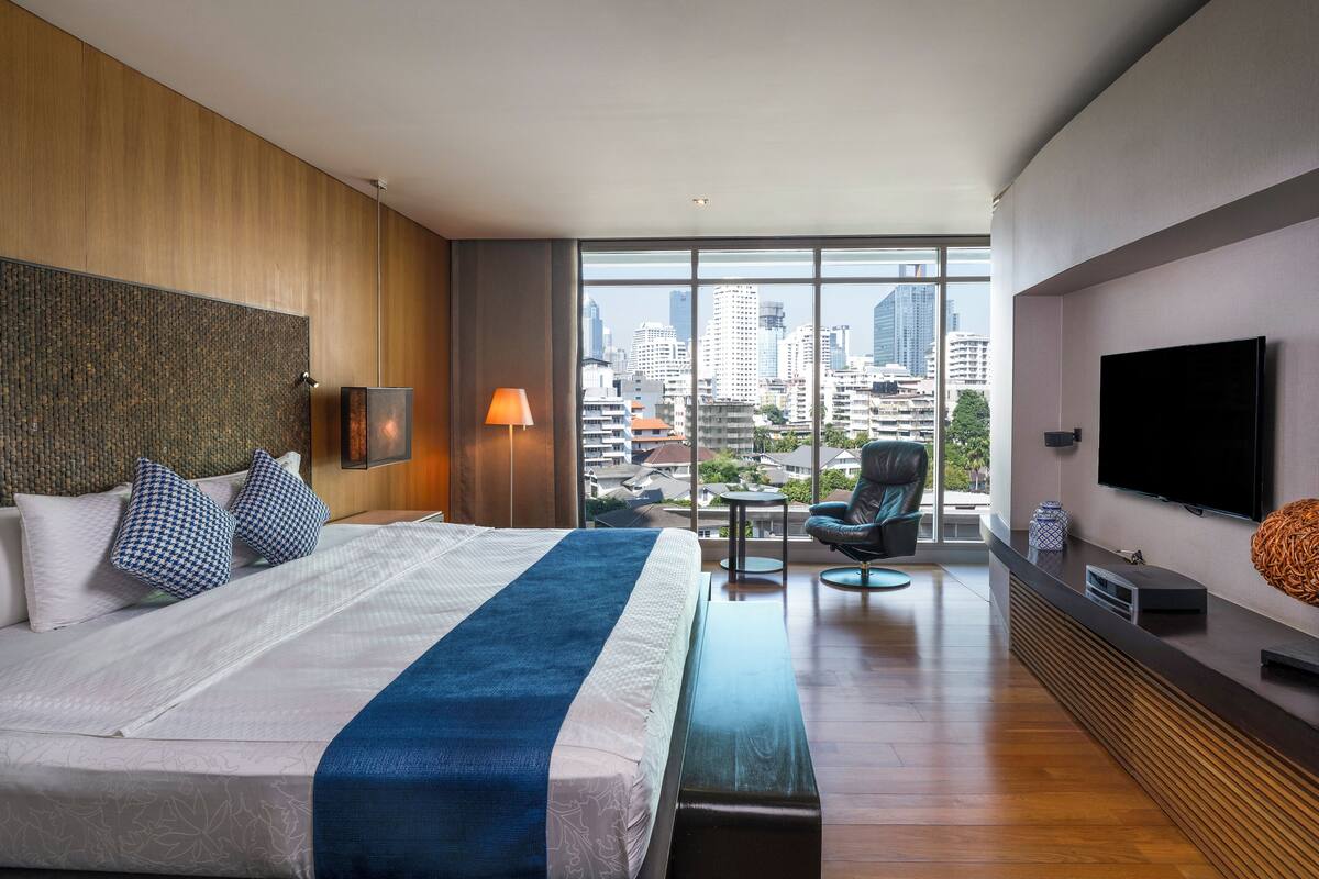 Une chambre d’hôtel moderne dotée d’un grand lit, d’une vue sur la ville, d’un téléviseur à écran plat et d’un coin salon.