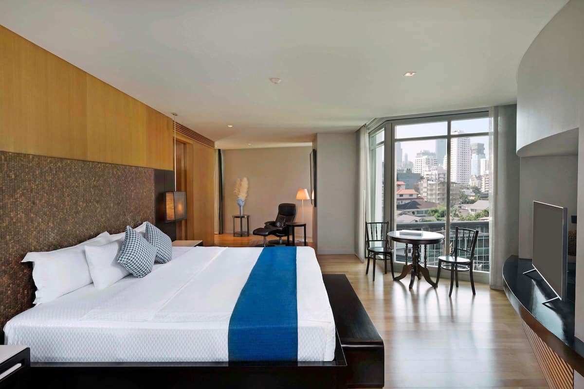 Une chambre d’hôtel moderne dotée d’un grand lit, d’un balcon offrant une vue sur la ville, d’un petit coin salon et d’un téléviseur à écran plat.