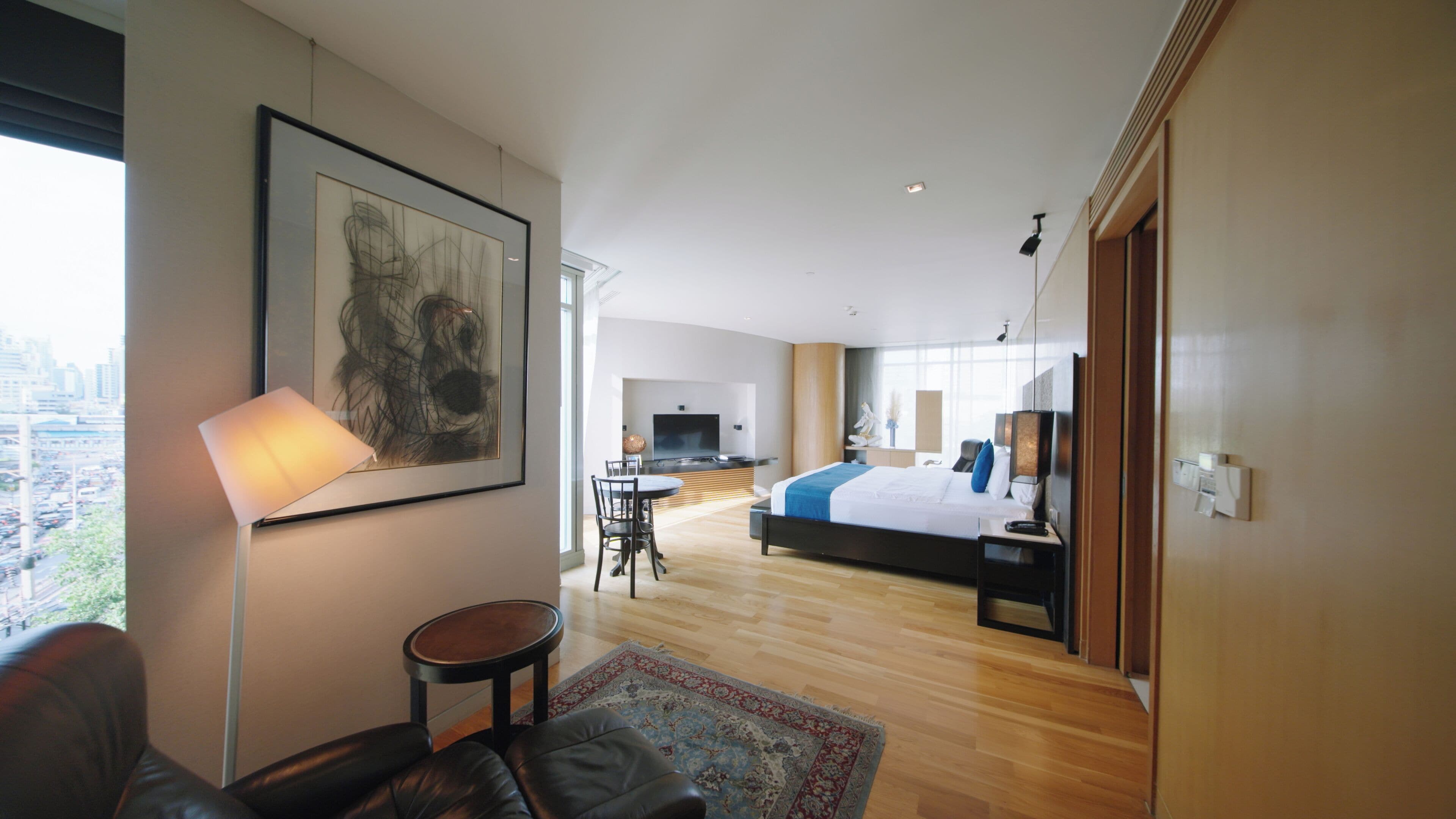 A modern hotel room with a large bed, a desk, and a television. There is a view of the city from the window.