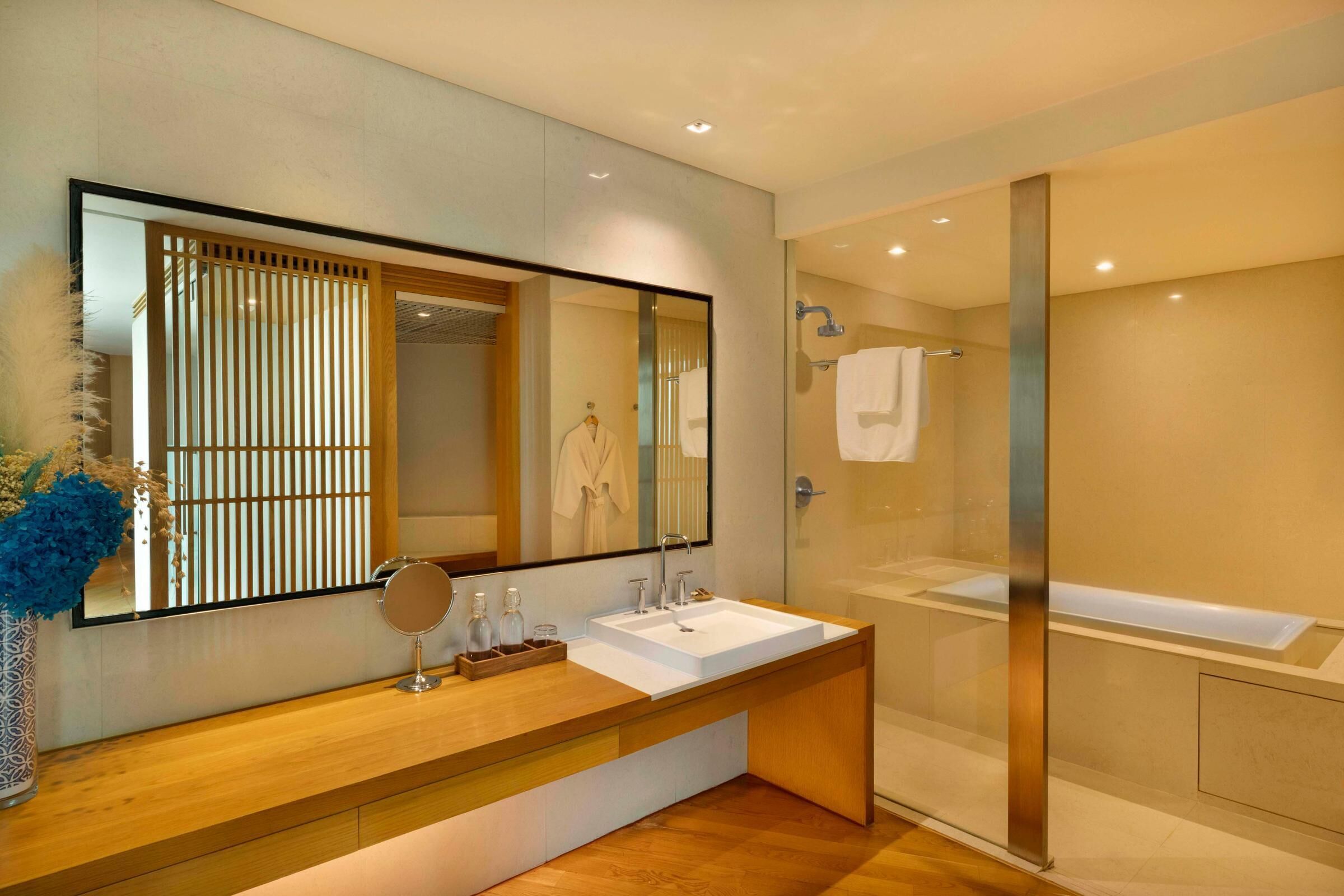 A modern bathroom with a large mirror, wooden vanity, and a glass-enclosed shower.