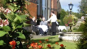 A garden setting with a brick building, outdoor seating, and a fountain.