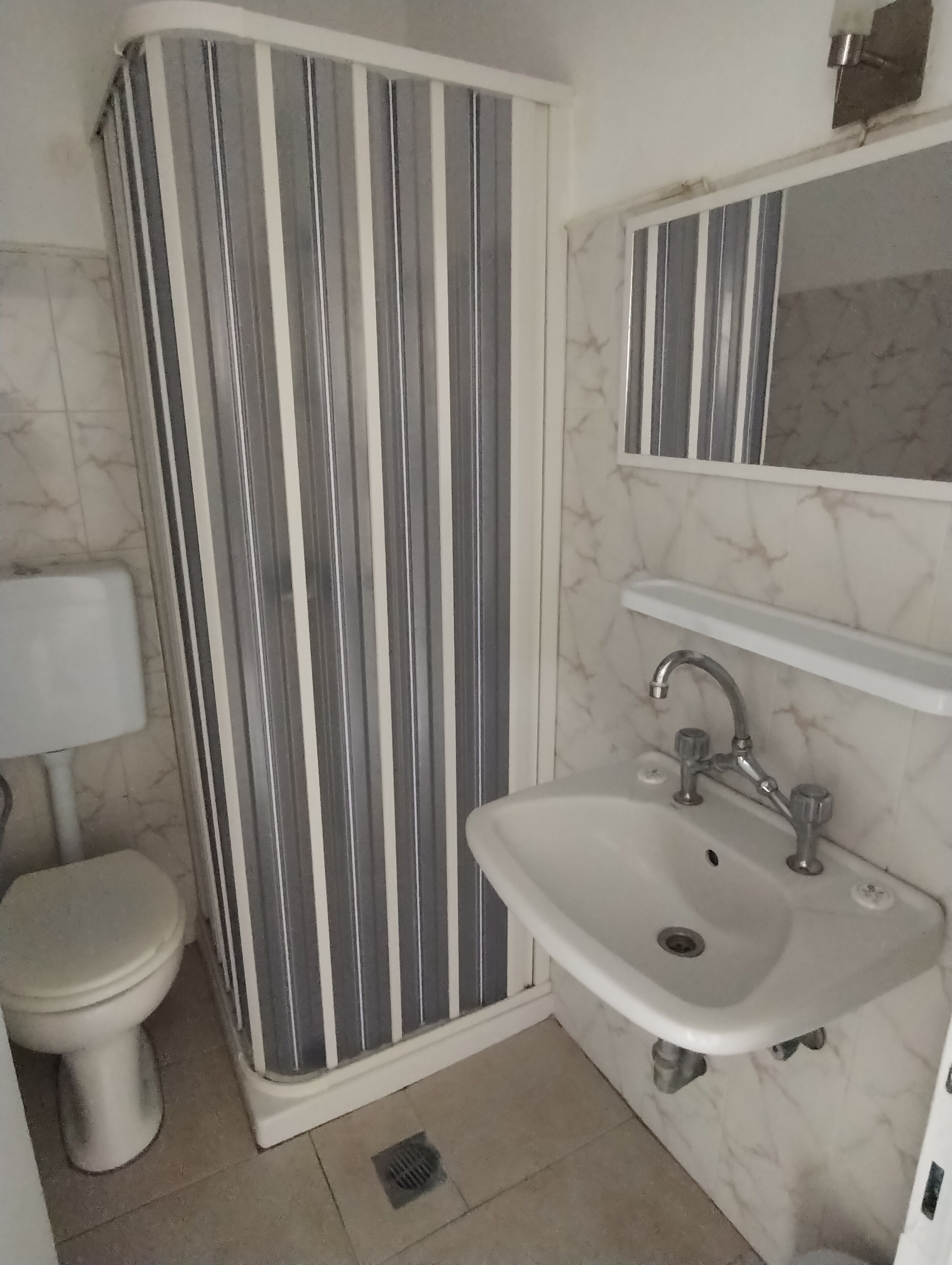 Ein Badezimmer mit gestreiftem Duschvorhang, einer weißen Toilette, einem Waschbecken mit Spiegel darüber und einer Wand mit Marmor-Optik.