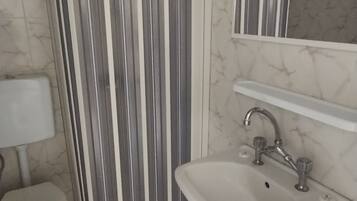 Ein Badezimmer mit gestreiftem Duschvorhang, einer weißen Toilette, einem Waschbecken mit Spiegel darüber und einer Wand mit Marmor-Optik.