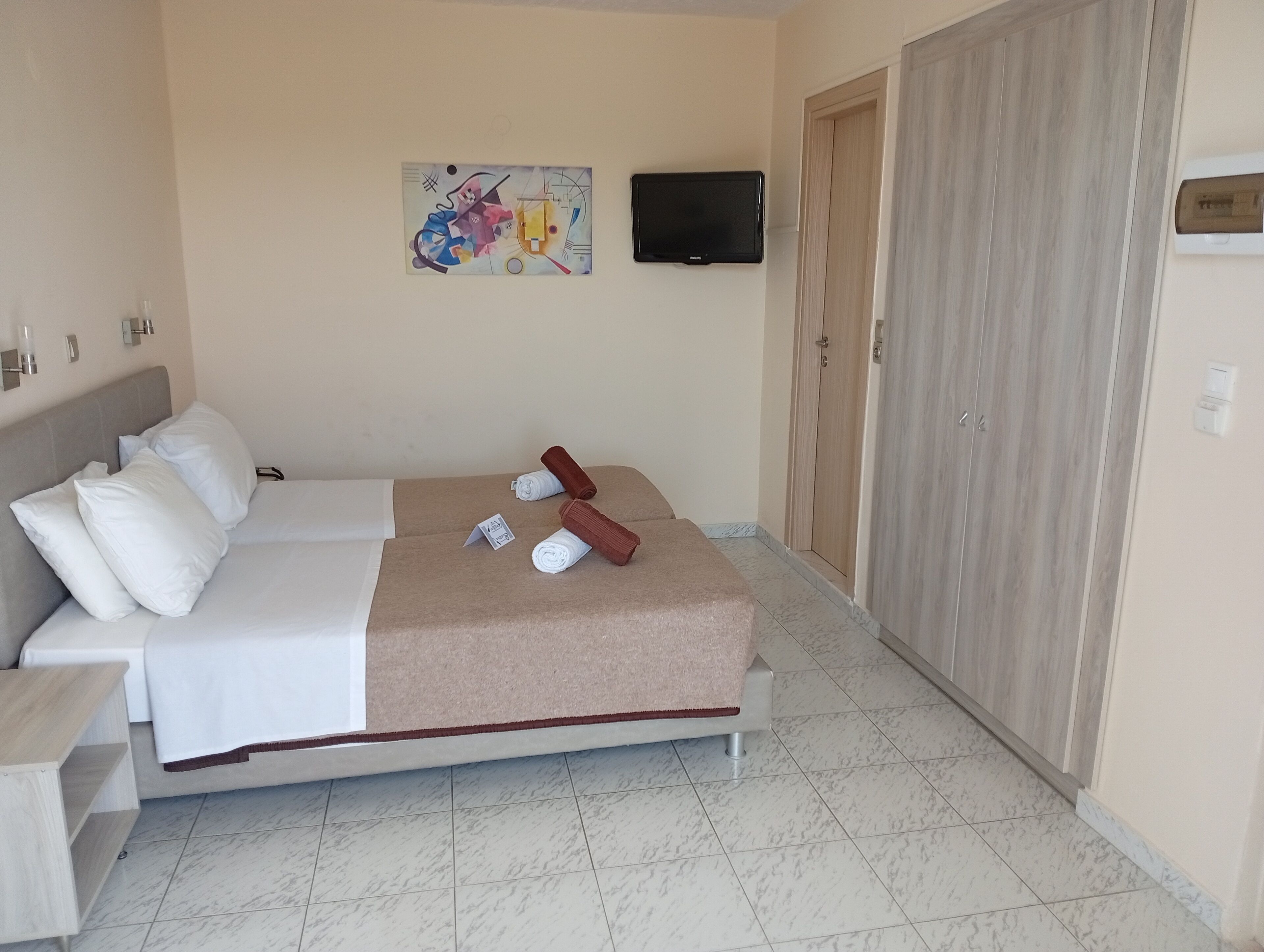 Una habitación de hotel con cama, televisión, un cuadro en la pared y un armario.