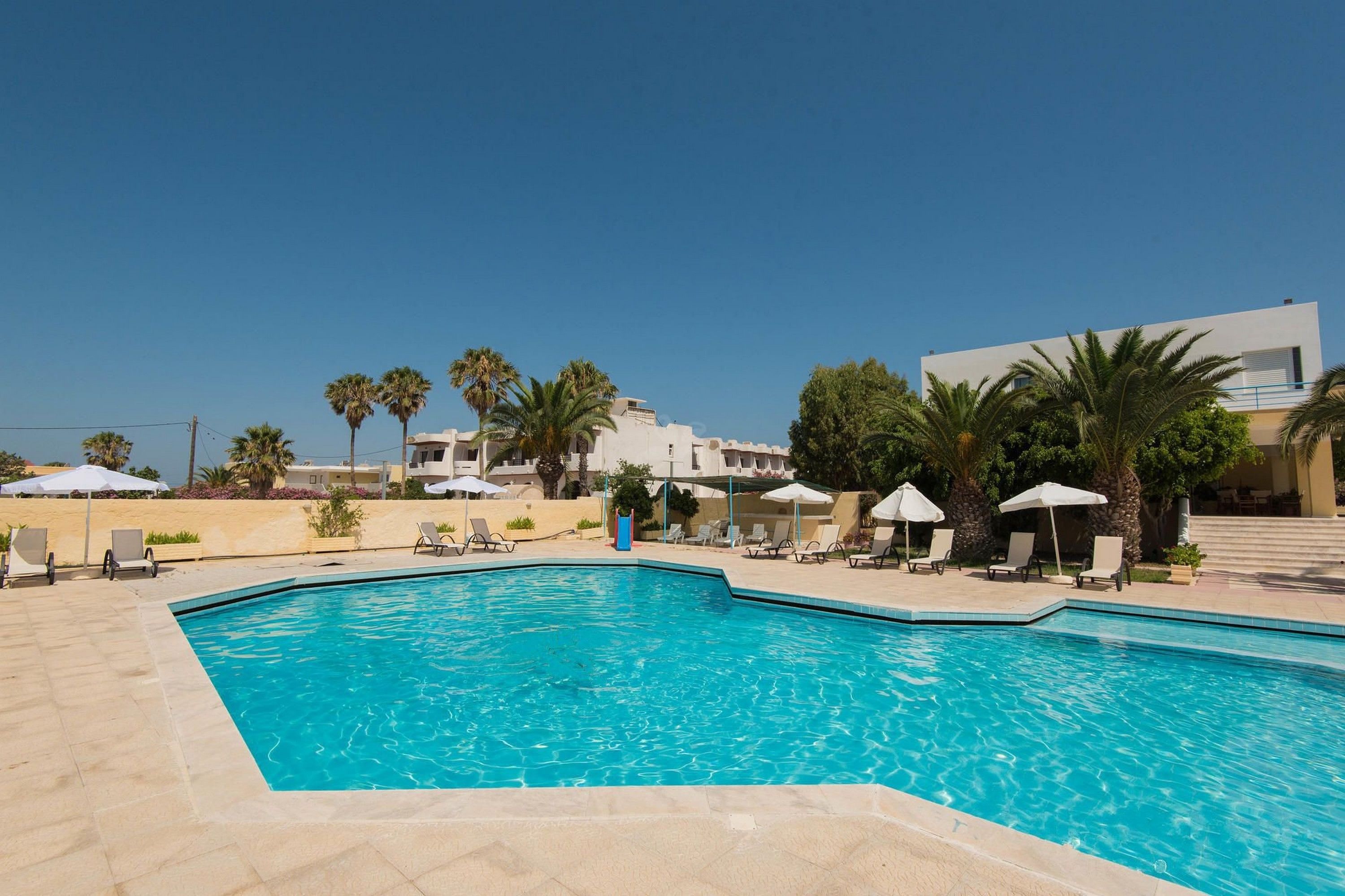 Una piscina al aire libre, sombrillas, sillones reclinables de piscina