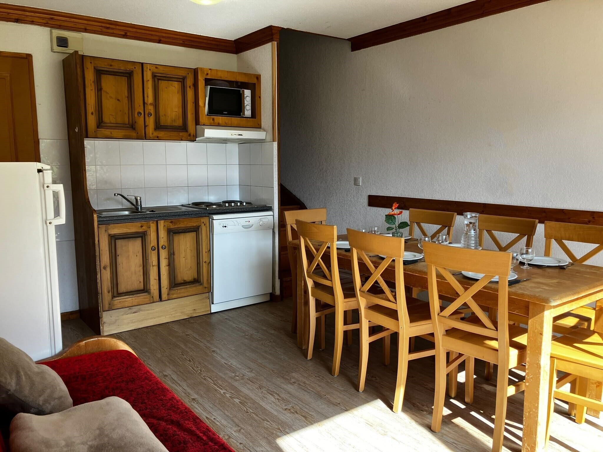 Ett kompakt kök med träskåp, en mikrovågsugn, en diskmaskin och en matplats med trästolar och ett bord.