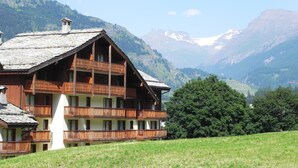 A wooden chalet with multiple balconies, set against a mountainous backdrop.