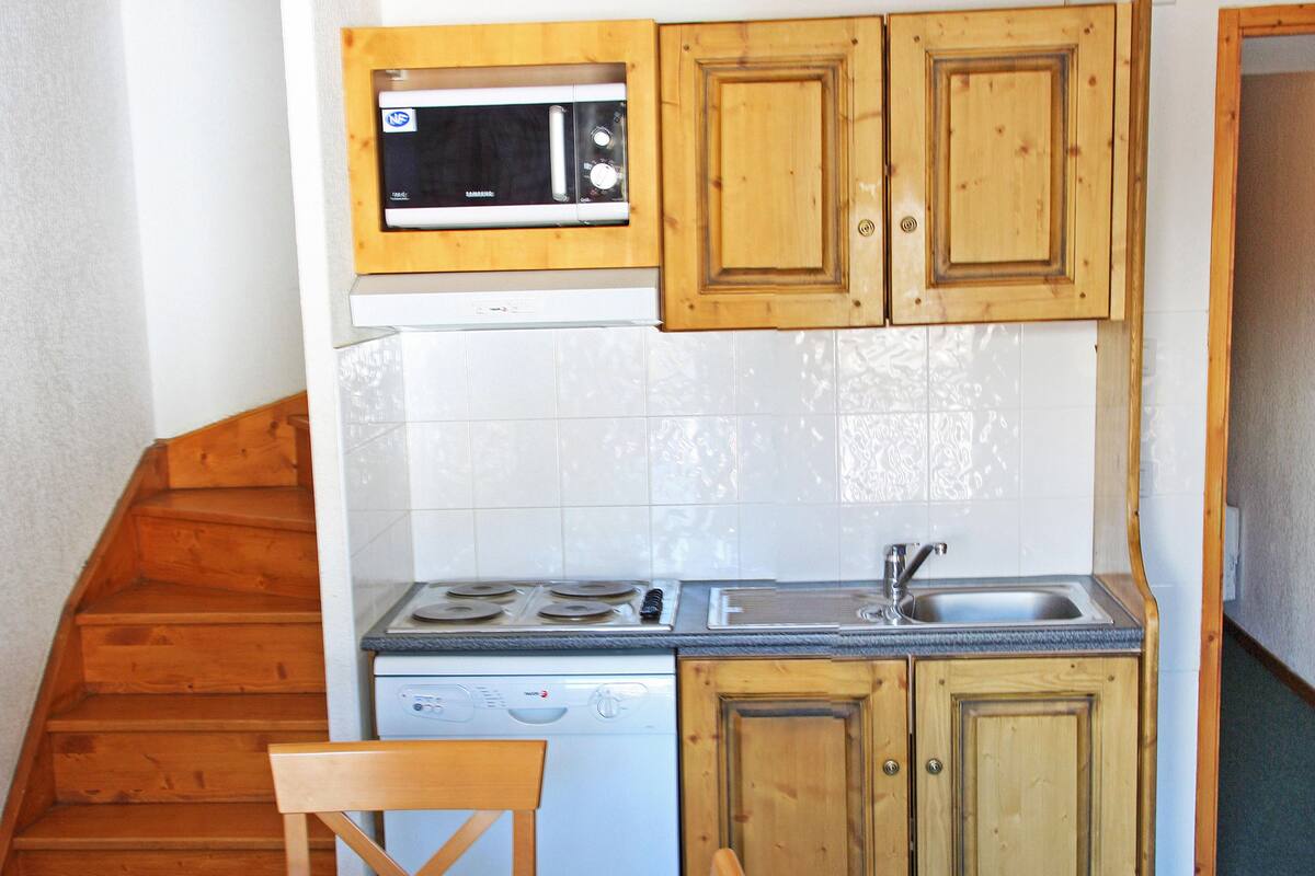 Une cuisine de taille réduite, dotée de meubles en bois, d’un four à micro-ondes, d’une cuisinière et d’un évier.