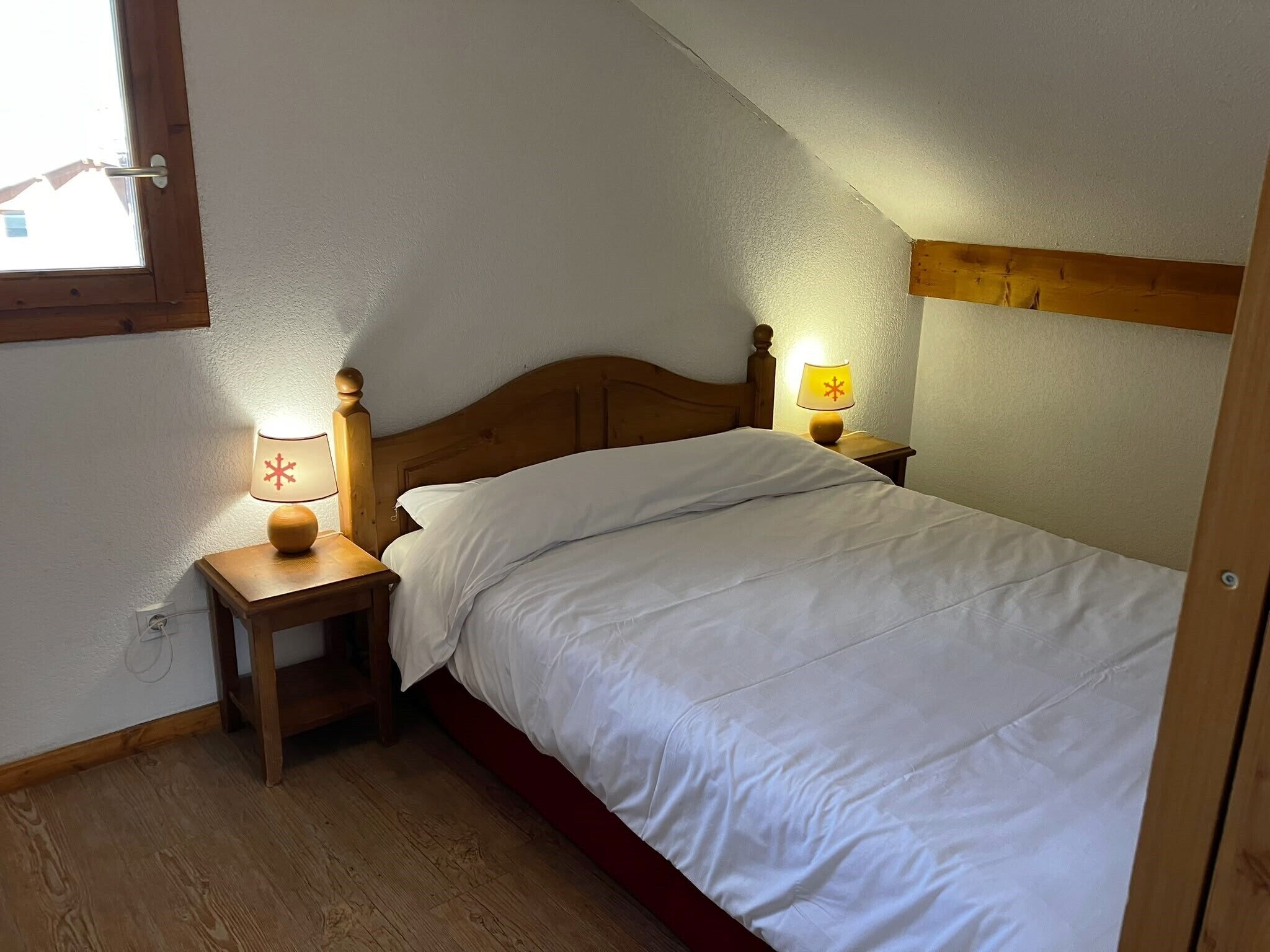 Een slaapkamer met een houten bed, twee nachtkastjes met lampen, een raam en een houten balk in het plafond.