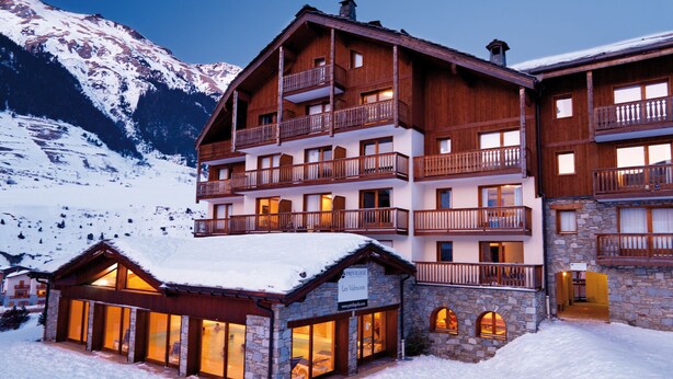 A multi-story hotel with balconies and large windows, surrounded by snow-covered mountains.