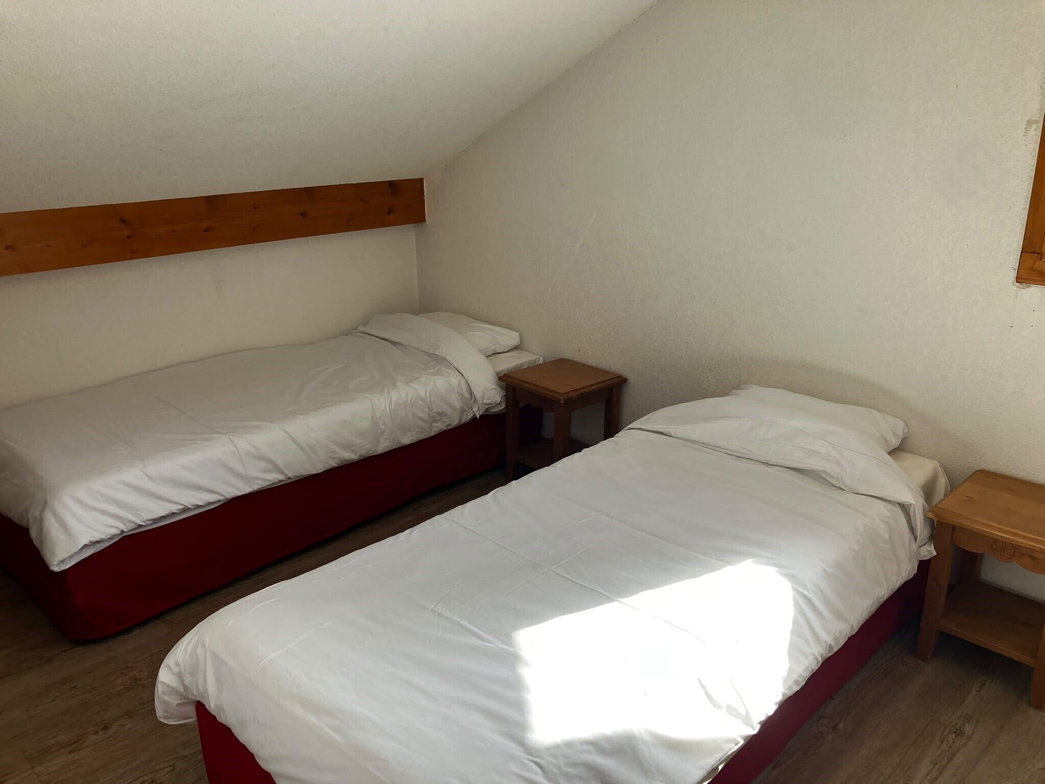 Un petit logement composé d’une seule pièce, comprenant deux lits simples, des têtes de lit en bois et un plafond en pente.