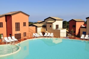 A swimming pool with white lounge chairs and a building with a red facade.