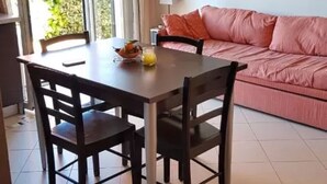 Een eetgedeelte met een tafel, stoelen, een bank en een aan de muur bevestigde televisie.