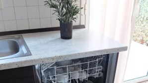 Een keuken met een vaatwasser, een spoelbak en een potplant op het aanrecht.