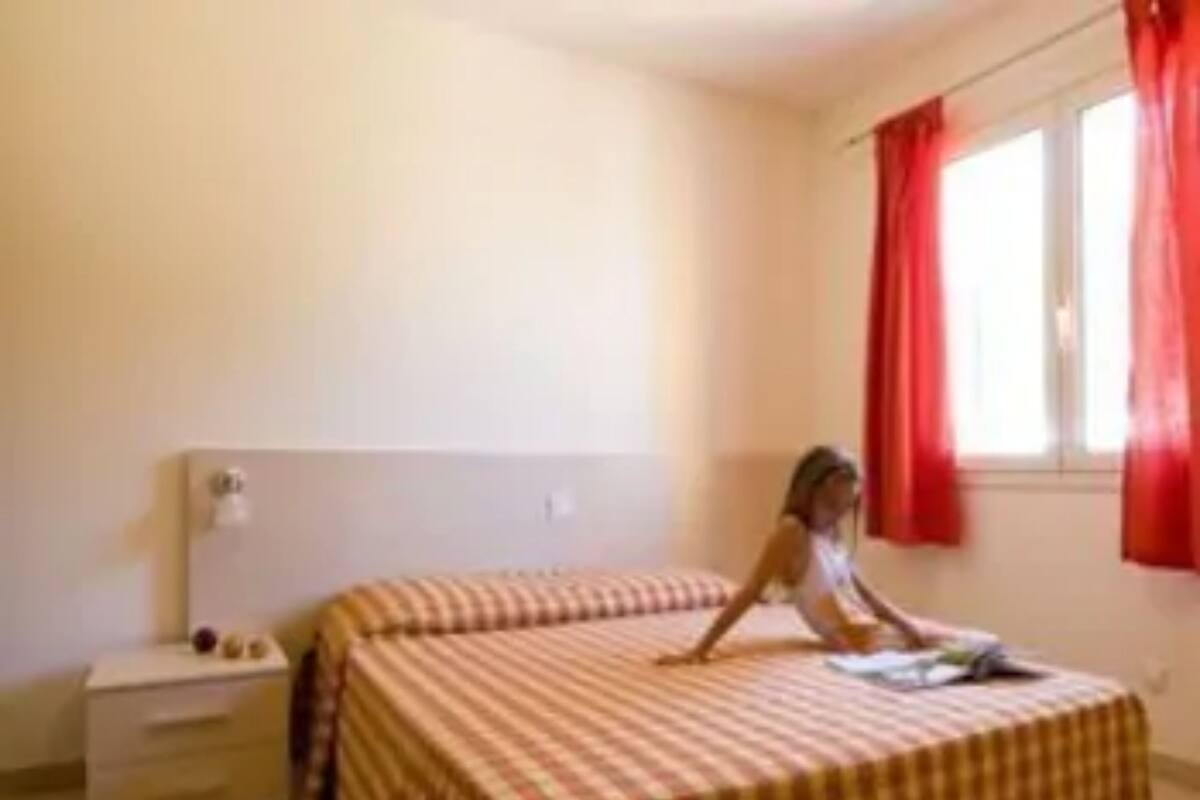 A room with a bed, a nightstand, and a window with red curtains.