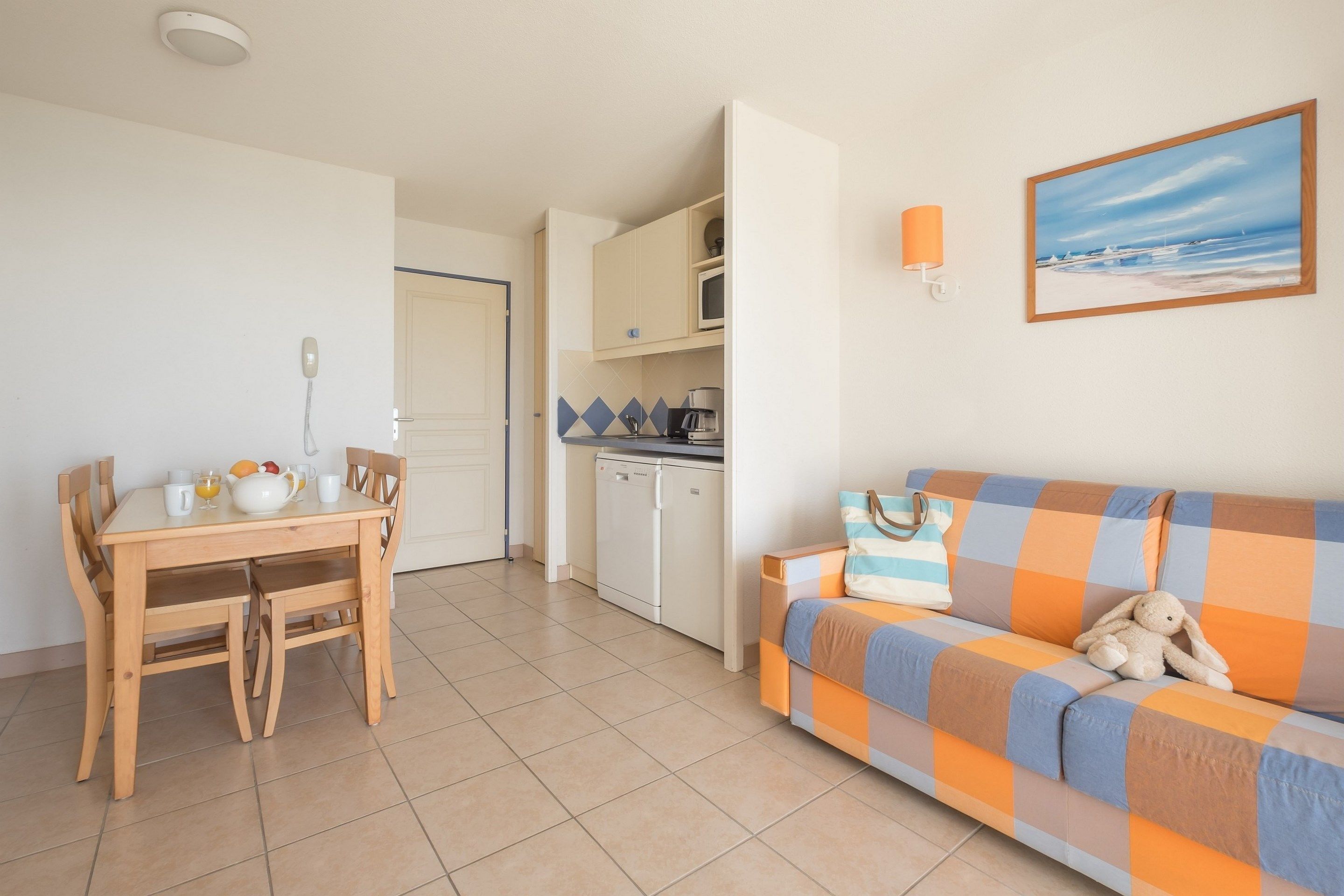 Een compacte leefruimte met een eethoek, kitchenette en een bank met een kussen.