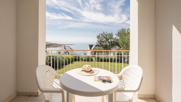 Een balkon met een witte tafel en twee witte stoelen, een hoed en een tijdschrift.