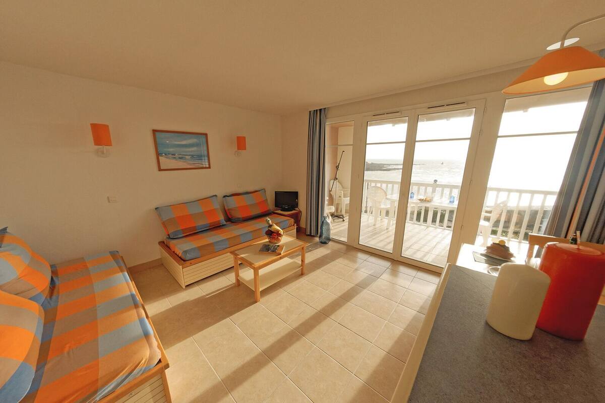 A living room with a sofa, a coffee table, and a TV. There is a balcony with a view of the sea.