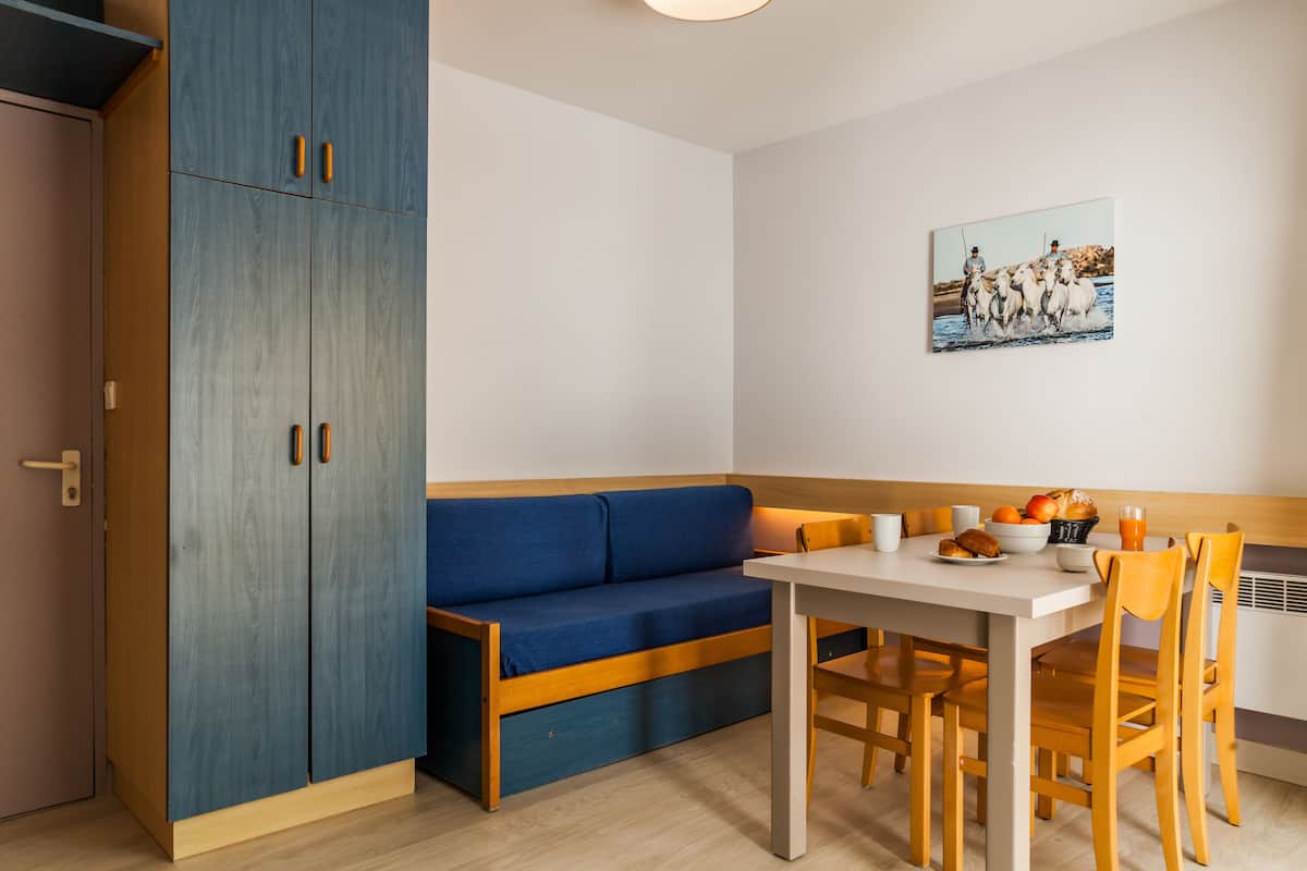 A compact room with a blue sofa, a dining table with chairs, and a large cabinet.