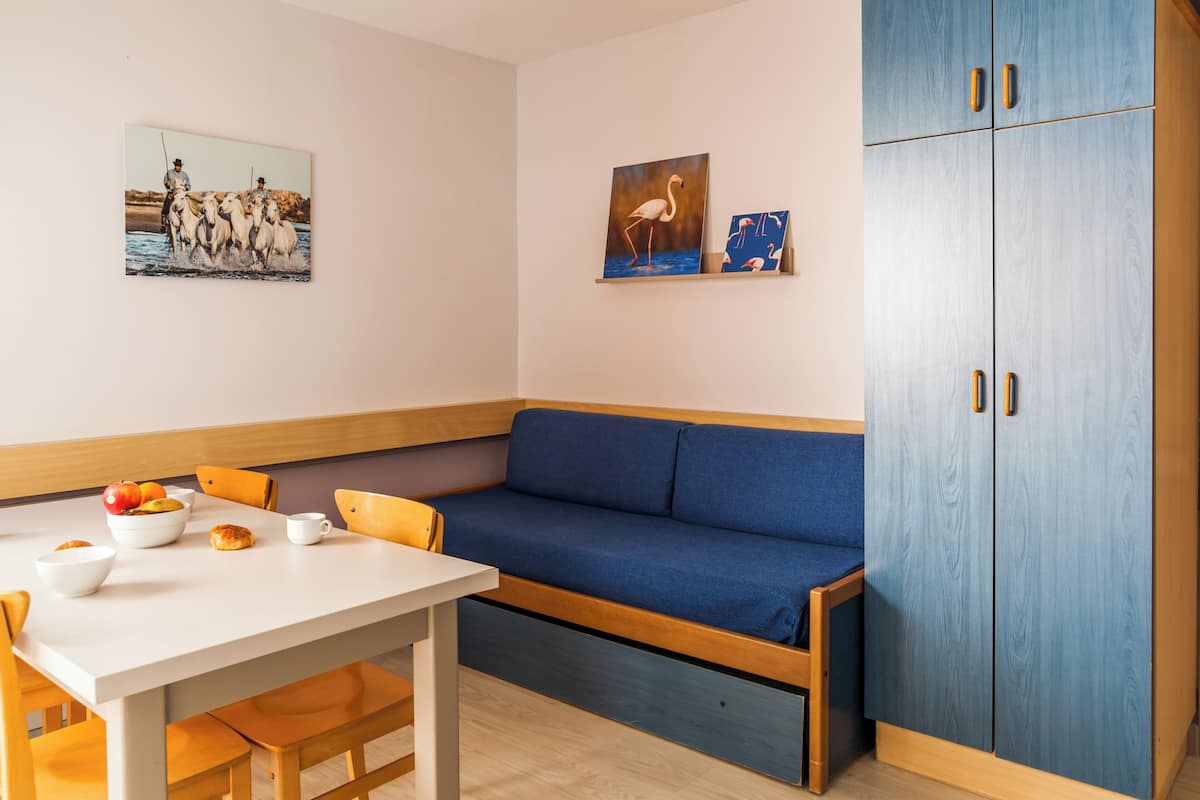 A room with a white table, blue sofa, wooden cabinet, and two wall-mounted paintings.