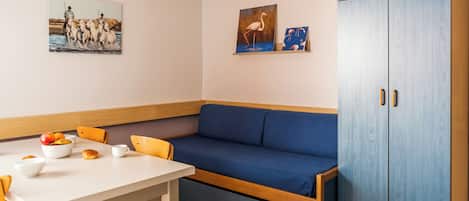 A room with a white table, blue sofa, wooden cabinet, and two wall-mounted paintings.