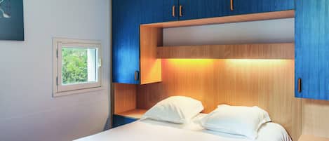 A bedroom with a bed, a nightstand, a window, and built-in wooden cabinets.