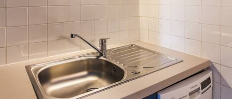 A kitchen with a stainless steel sink, a dishwasher, and white tiled walls.