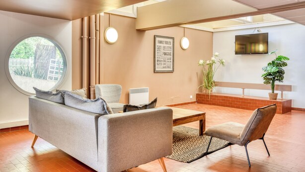 A modern living room with a sofa, armchairs, a coffee table, a TV, and a large window. - Résidence Pierre & Vacances Les Terrasses Du Parc (La Grande-Motte)