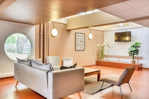 A modern living room with a sofa, armchairs, a coffee table, a TV, and a large window.