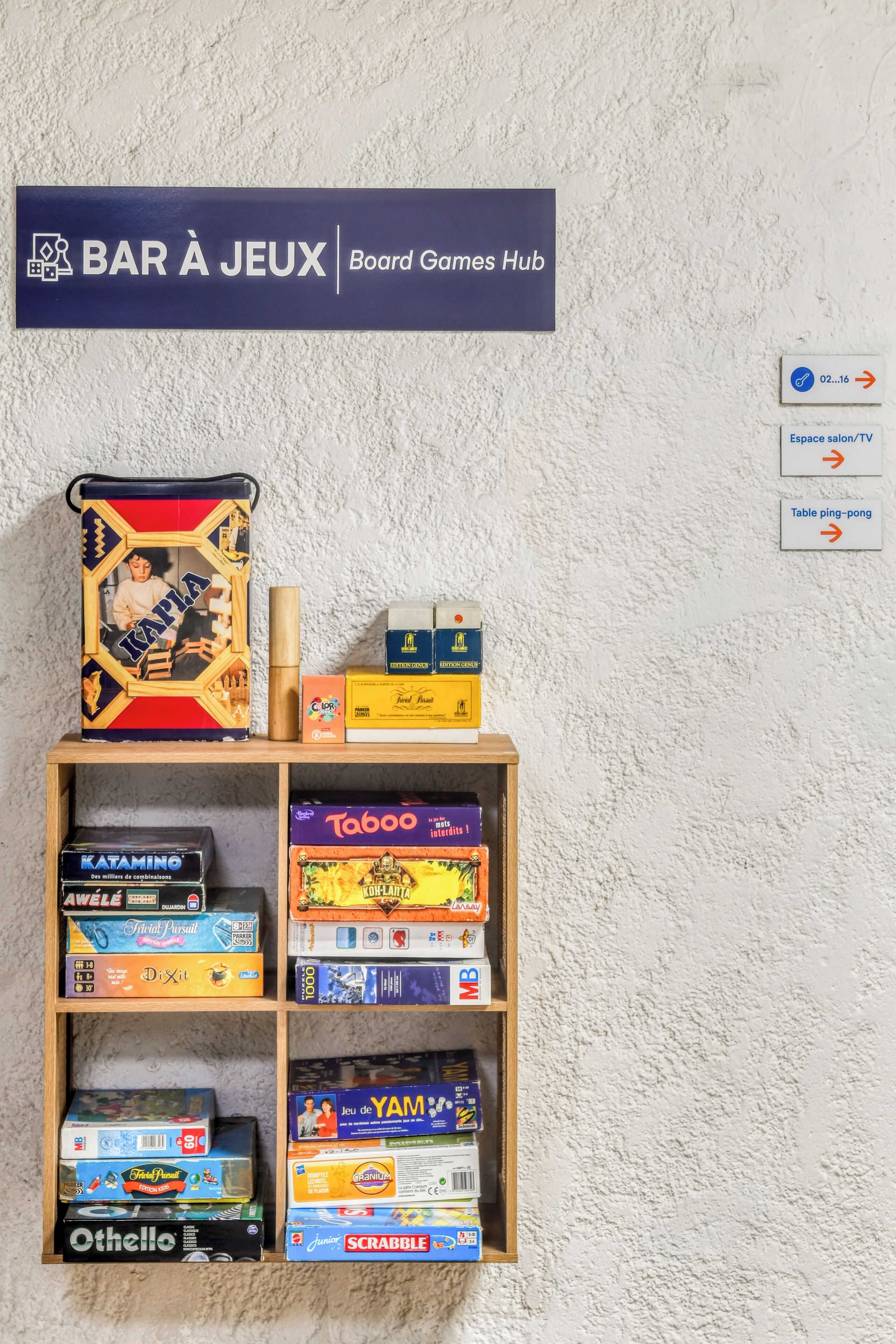 Ein Regal mit Brettspielen und eine Beschilderung darüber mit der Aufschrift 'BAR À JEUX Board Games Hub'.