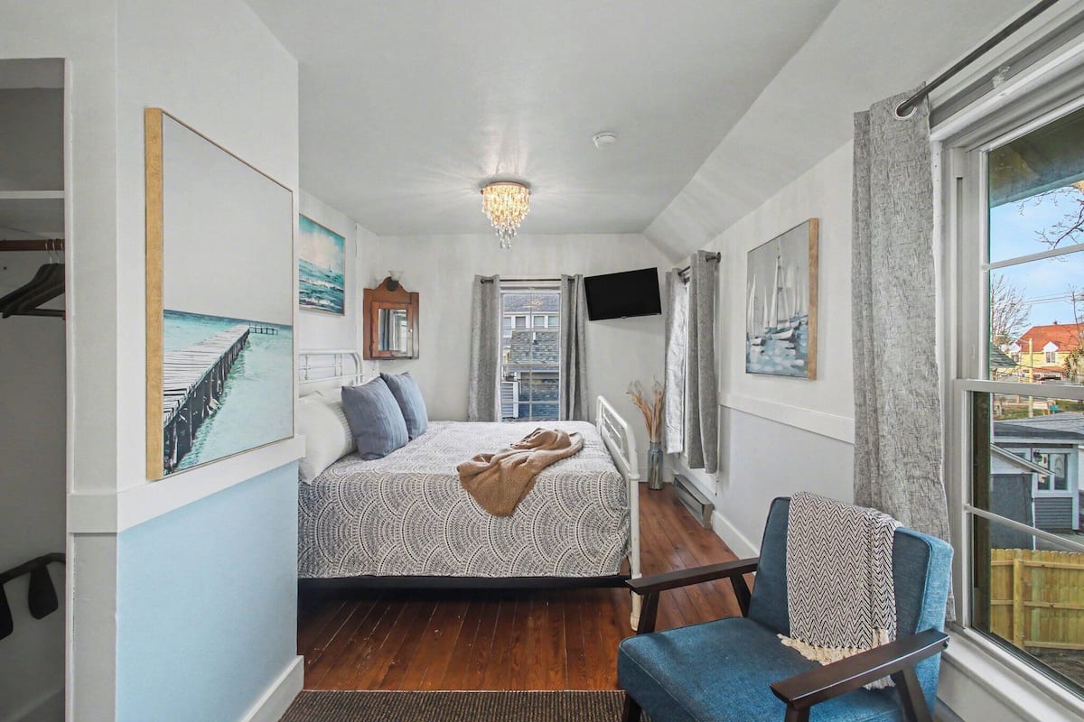 A bedroom with a bed, a chair, a TV, and artwork on the walls.