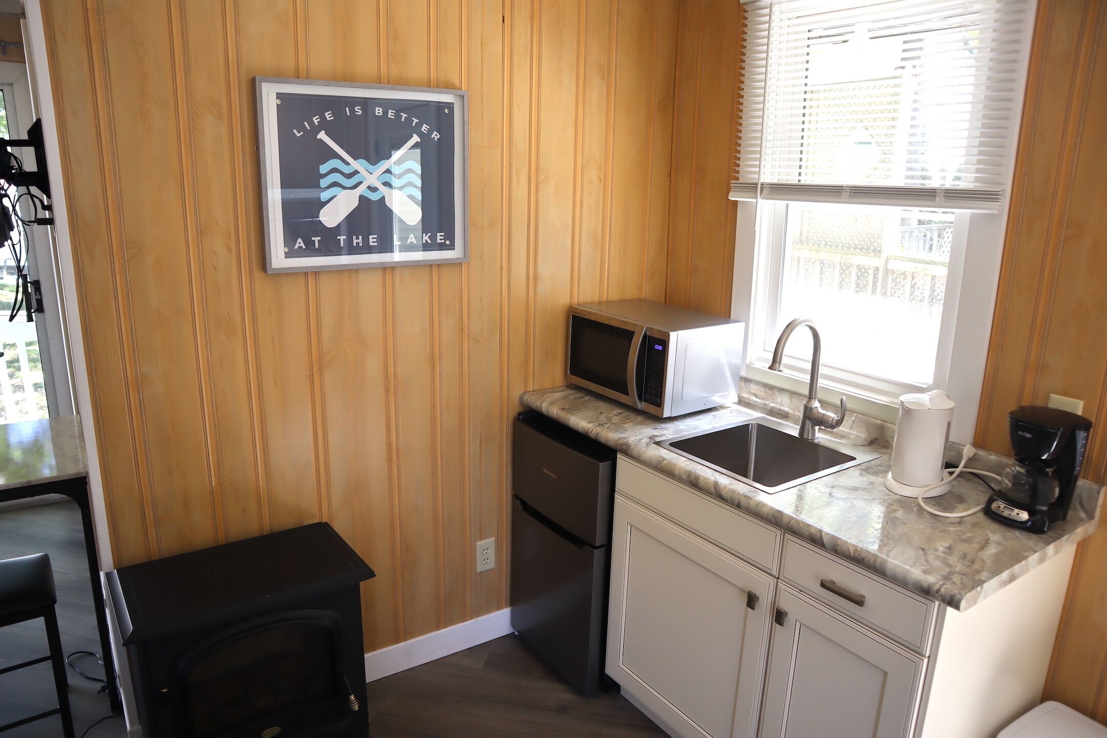 A compact kitchen with wooden paneling, a microwave, a sink, and a coffee maker.