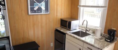 A compact kitchen with wooden paneling, a microwave, a sink, and a coffee maker.